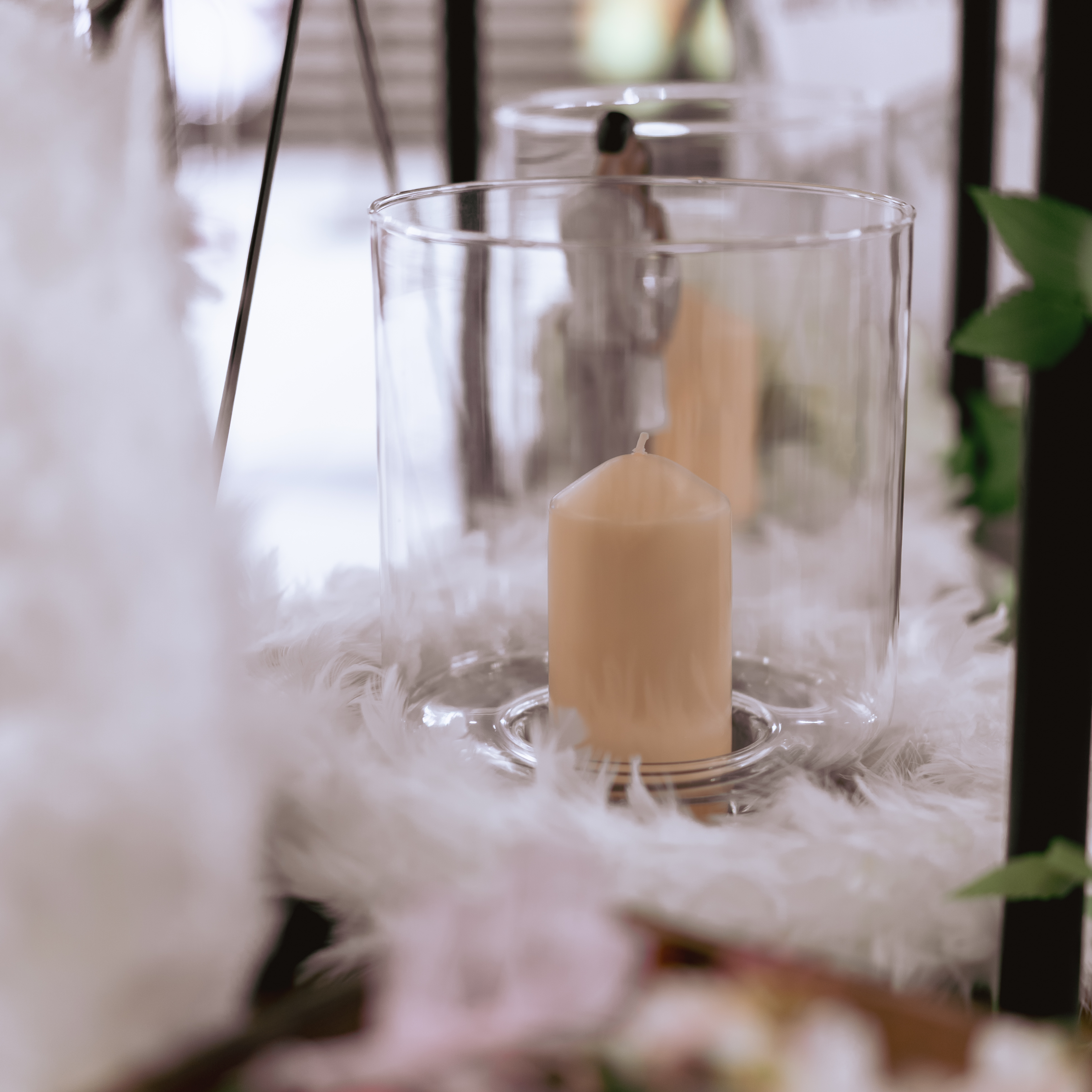 Glasvase mit Kerze umrahmt von weißem Federkranz 